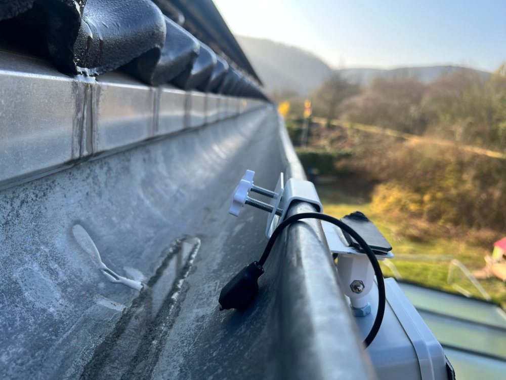 Probe lying on the gutter bottom, cable looped over the front edge, clamp bracket with two thumbscrews